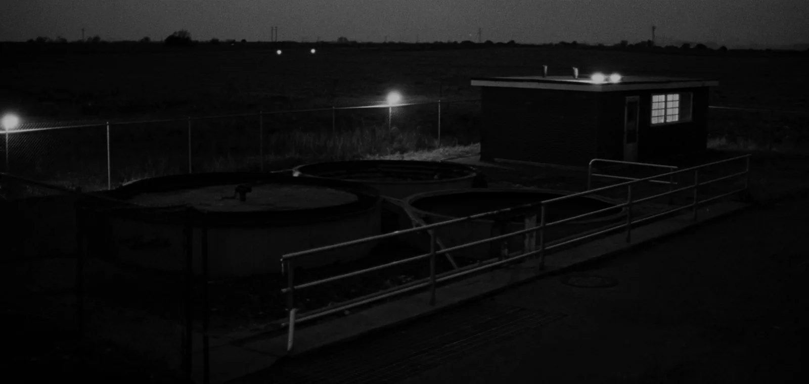 A small rural drinking water treatment plant at dusk, with circular concrete clarifier basins, galvanised handrails and a low pump house.